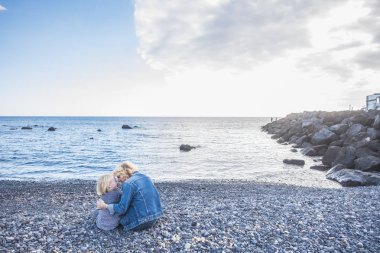 Mutlu aile çifti anne plajda oturuyor açık hava aktivitesinin tadını çıkarıyor ve sonsuza dek sevgi ve şefkat içinde sakin denize bakıyor.