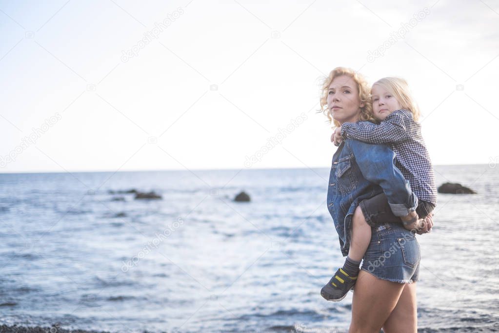 beautiful young mother and little child blonde too walking at the beach in happiness