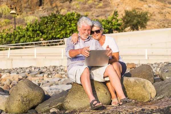 happy senior couple with tablet pc computer on pebble beach laughing and joking