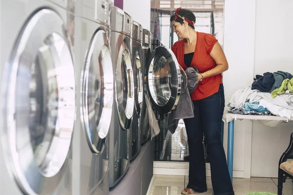 brunette woman washing and cleaning some dresses and clothes at laundry mat service automatic machine