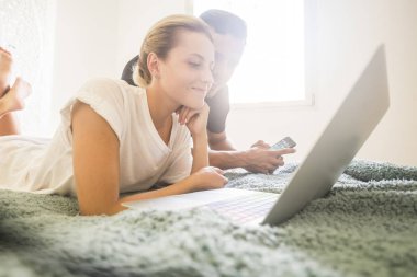 yatakta döşeme ve yatak odasında dizüstü bilgisayar üzerinde çalışan genç çift