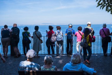 Turistler için büyük bir terasta deniz manzarasının tadını çıkaran bir grup insan. Sırt çantalı turizm kavramı ve keşfetme ve seyahat etme zevki, modern yaşam tarzı ve tatil kavramı