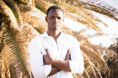Güzel, yakışıklı siyah ırkın portresi. Afrikalı genç adam kameraya bakıyor. Kollarını kavuşturmuş duruyor.