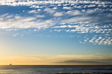Okyanusta gün batımında feribot gezisi ufukta geziniyor ve bazı sörfçüler suda. 