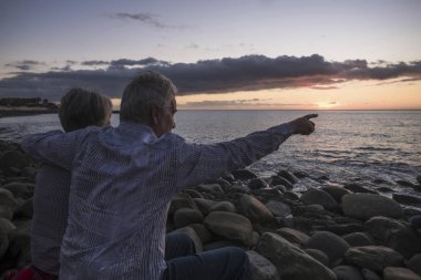 oturan ve her diğer deniz günbatımı arka plan üzerinde bakarken sarılma yaşlı çift