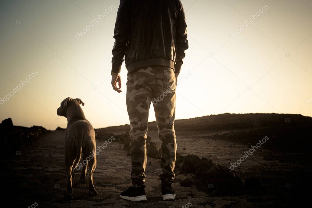 Lonely man and best friend dog walking together on a path in outdoor desert leisure activity with ocean in background at the end - friendship and travel concept for people with animals
