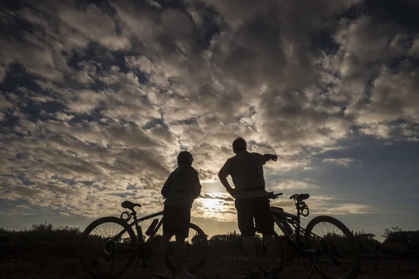 silhouettes of people riding mountain bikes on dramatic cloudy sky background
