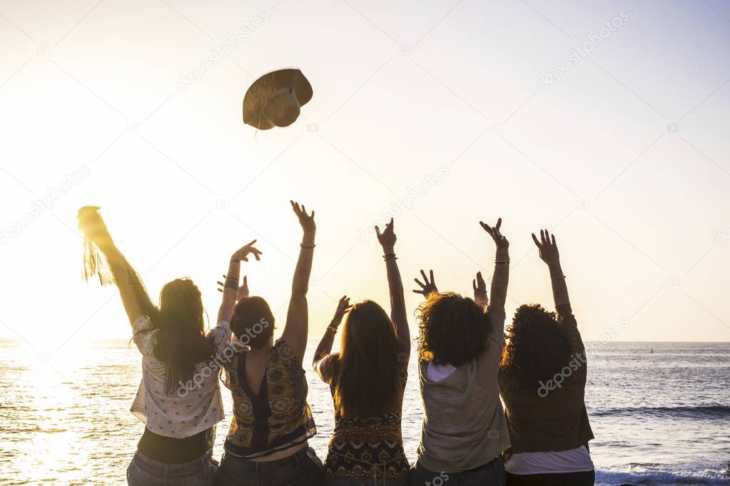Summer and happiness for travel and friendship concept with group of happy girls viewed from rear enjoying and celebrating the sunset and the sea together launching hat and giving up