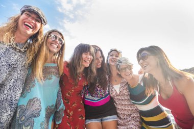 Yedi güzel beyaz kız grubu gün batımında eğleniyor, gülüyor ve gülümsüyor. Arka planda yaşayan insanlar arkadaşlığın tadını çıkarıyorlar.