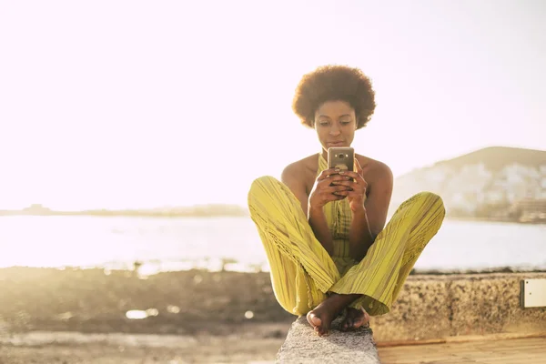 Giovane Bella Ragazza Africana Utilizzando Smartphone Mentre Seduto Spiaggia Foto Stock Royalty Free