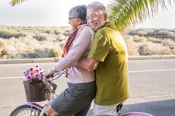 aged couple laughing while riding on bike, outdoor leisure activity