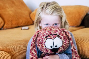 Üzgün genç çocuk sarı saçlı köpek yavrusuna evde sarılıyor, beyaz çocuk konsepti ve bir aile içinde oğul koruması.