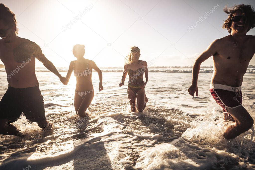 Group of beautiful millennial alternative young people have fun and enjoy the summer holiday vacation together in friendship running in the water of the ocean