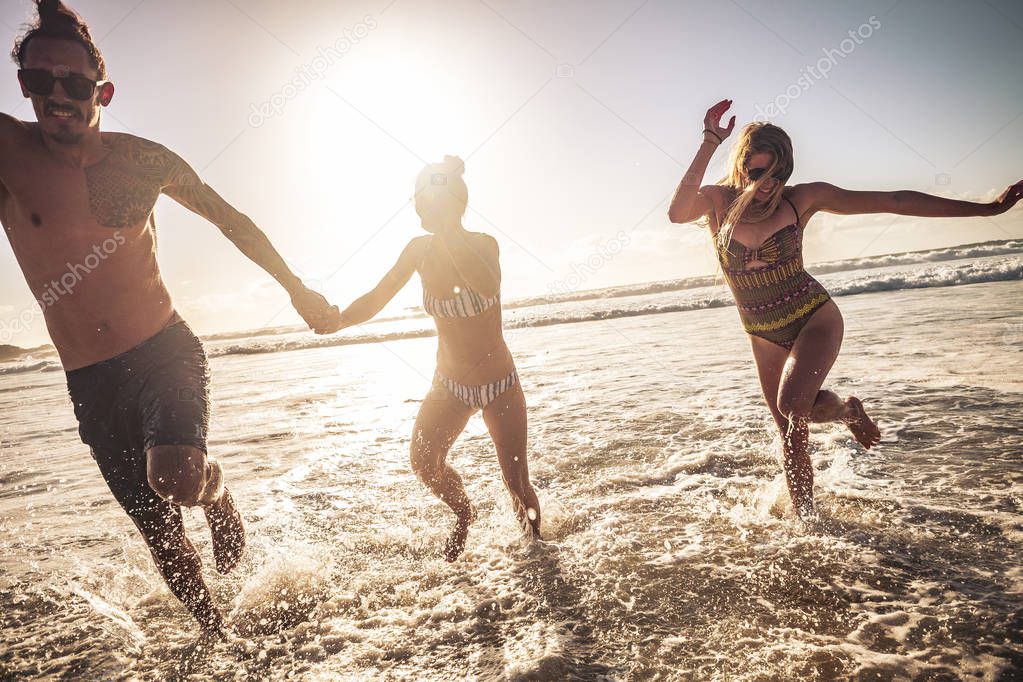 Friends caucasian group of people man and two women enjoy and have fun together in friendship during summer vacation running out of the water