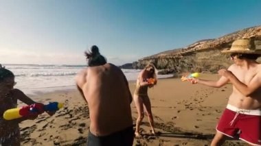 Genç ve insanlar tatil sırasında plajda su tabancaları ile oynuyor 