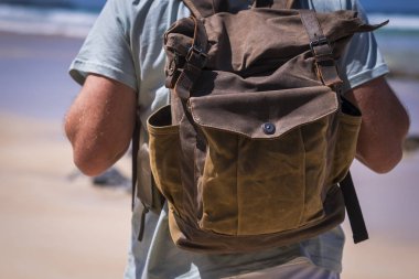 İnsan ve deri bir sırt çantasıyla seyahat ve tatil hayatı kavramı arka planda gökyüzü ve plajda boş zaman aktiviteleri için izleniyor.