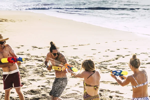 Youthful and people playing with water guns at beach during vacation