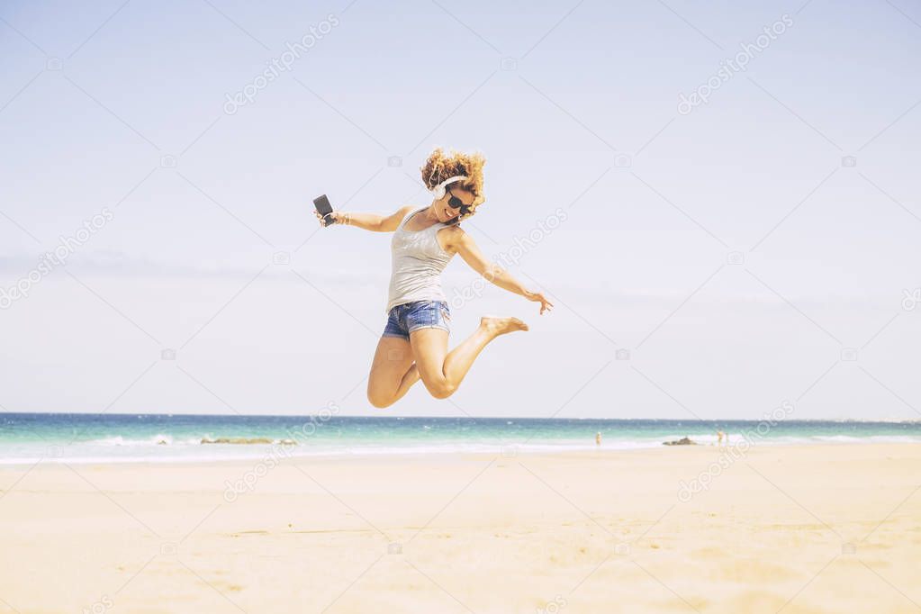 Pretty girl with curly hair and short jeans enjoying at beach while listening music 