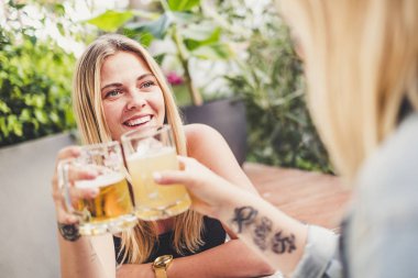Cheerful blonde with friend at the bar drinking beer and celebrating in friendship toasting the glasses and having fun together - happy people celebrate with friends