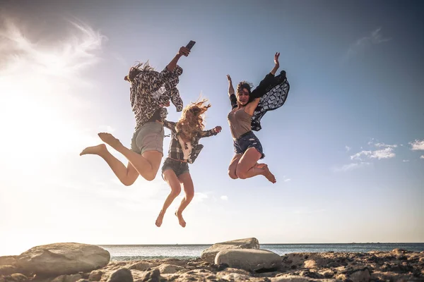 一群年轻人一起庆祝友谊 在海滩上欢欢欢喜喜地跳着 背景是大海和日落 — 图库照片