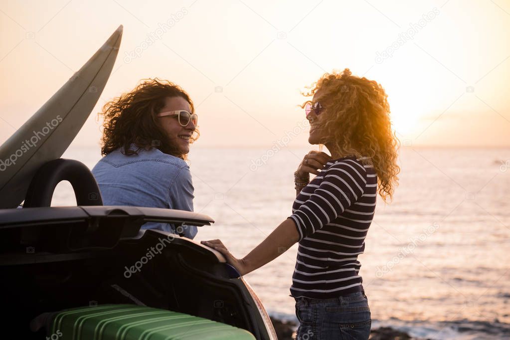Beautiful people couple of friends curly lady enjoying travel together and have fun with the sunset on the ocean - summer holiday vacation concept with happy females and car and luggages