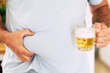 Fat belly for junk food or beer beverage concept with middle age man taking his belly and showing a pint of beer clipart