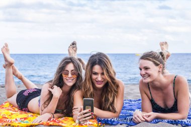 Arkadaşlık içinde üç güzel kız grubuyla yaz konsepti. Plajda uzan ve rahatça konuş ve akıllı telefon kullan. 