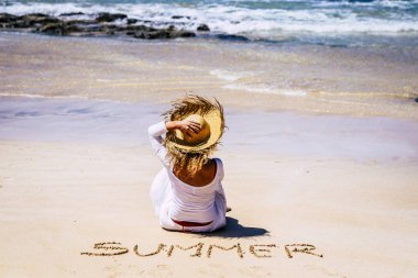 kum üzerinde oturan ve plajda rahatlatıcı şapkalı kadın arka görünümü 