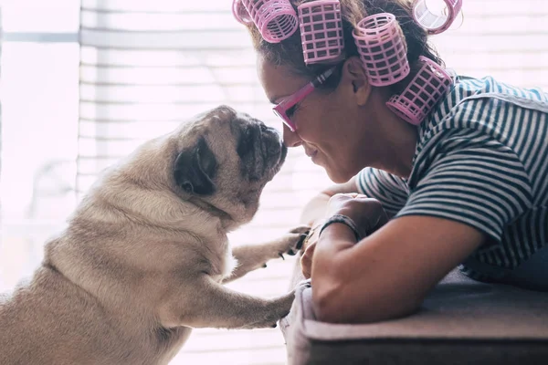 young woman lay down on sofa at home and lovely adorable pug dog kissing her on nose