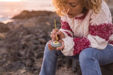 woman painting stone with mandala at seashore  
