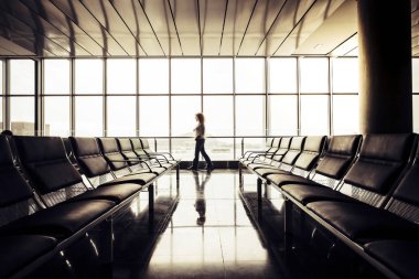 Büyük pencerenin yakınındaki boş kapılarda gergin bir şekilde yürüyen bir kadın. 