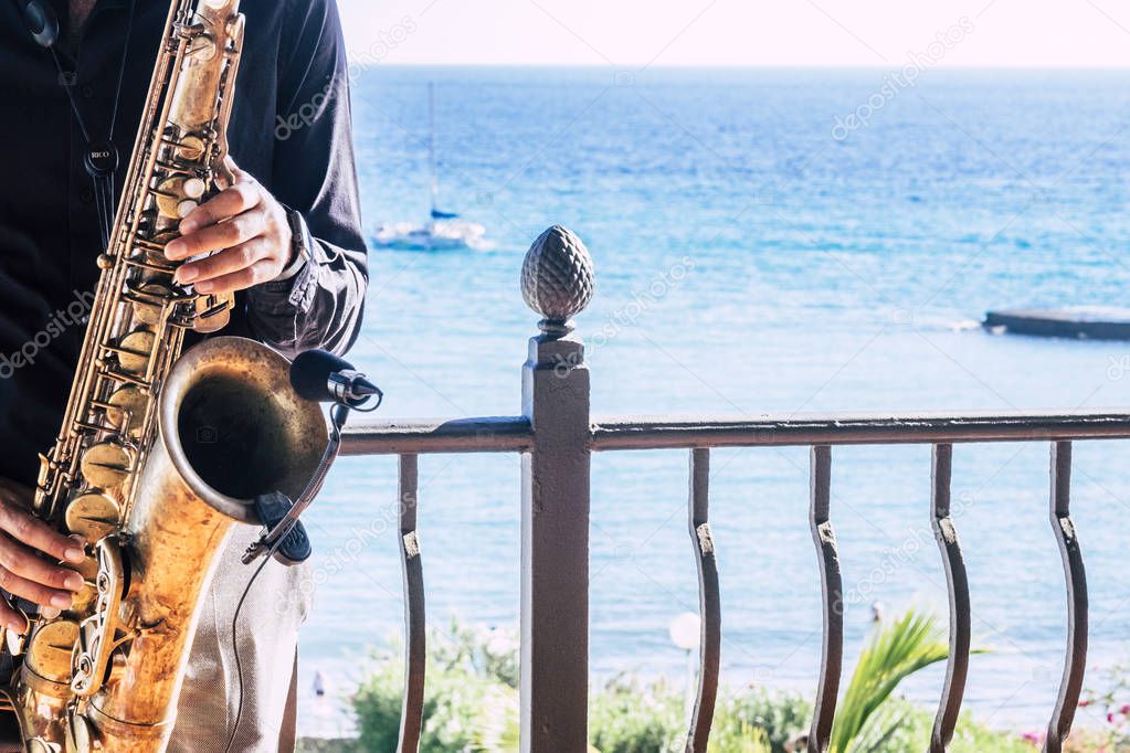 closeup of music artist saxophonist  touching his instrument in the restaurant or bar with the beach or the sea or ocean in the background