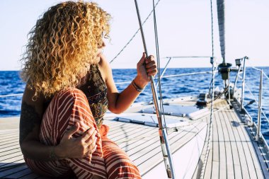 Travel and luxury lifestyle concept wtith beautiful blonde curly attractive woman sitting on dock of a sail boat  clipart