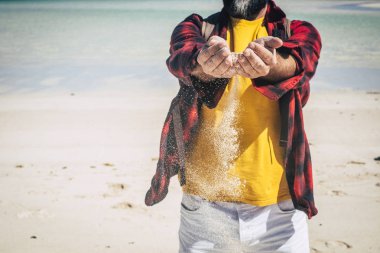 İnsanın ellerine yakın çekim, kumların düşmesine izin ver. Kumsalda tek başına eğlenen ve kumlarla oynayan bir yetişkin.