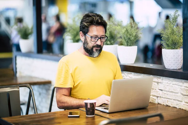 Bearded hipster man working at the laptop computer in the coffee bar with internet wifi connection free