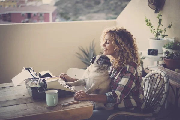 woman with pug sitting and writing with type machine in terrace of her house