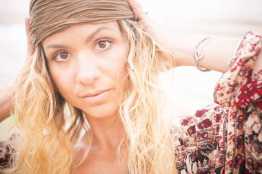 Güzel bir kadının kameraya baktığı ve sessizce poz verdiği bir sahne. Sarışın ve kıvırcık saçlı kadın. Moda çeşitliliği olan modern insanlar.