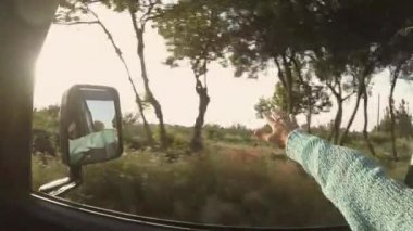 Yolda giderken rüzgarla oynayan kadın ve pencerenin dışında renkli günbatımı manzarası.
