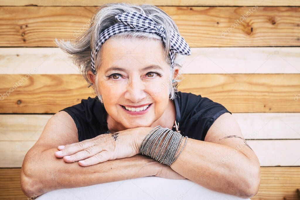 Portrait of cheerful caucasian senior happy woman with wood background - alternative and young old female smile and enjoy - tatooed skin for diversity concept and age - youthful lifestyle