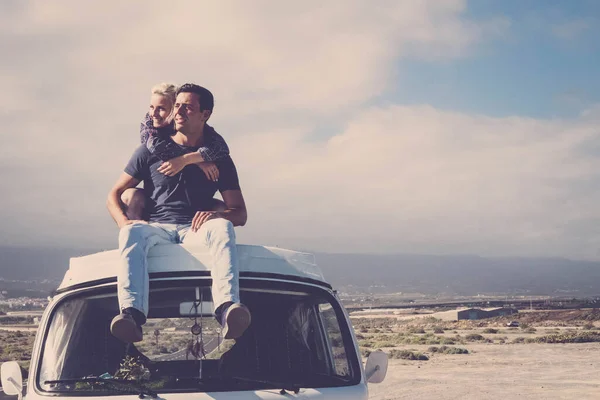 Love and travel with romantic wanderlust young people couple hug and stay together on an old vintage van rooftop enjoying romance and relationship