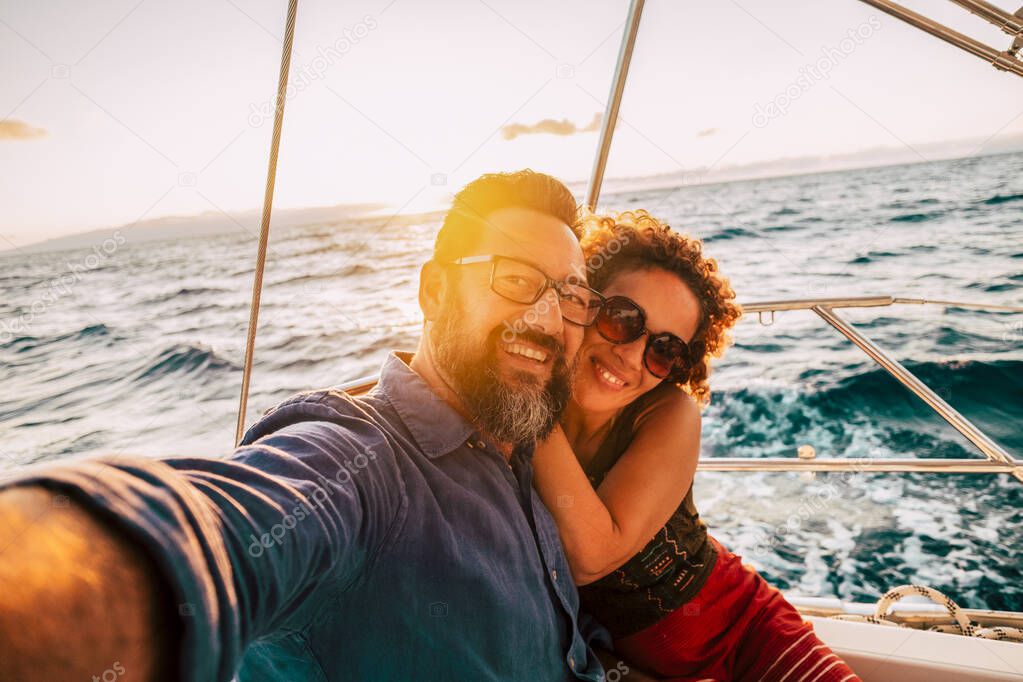 Adult happy couple take selfie picture yachting on a boat enjoying the sunset on the ocean 