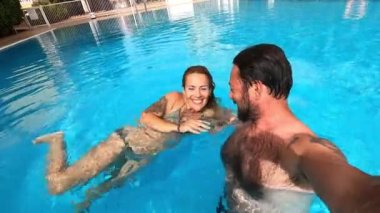  Olgun erkek ve kadın kamerayla havuzda yüzüyor.