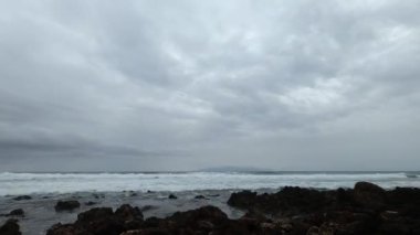 Bulutlu arka planda deniz ve kayalık kıyı şeridi zaman aşımı 