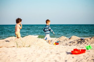 Kum ile deniz kumsalda oynarken çocuklar. Çocuk gökyüzüne karşı kıyı boyunca çalıştırın. Çocuk doğada iyi eğlenceler. Tatilde iki kardeş.