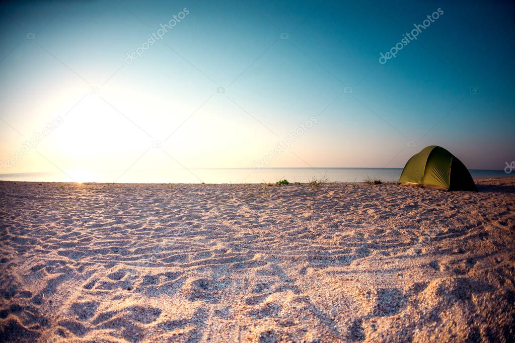 Green tent on the beach. Sunset on the sea coast. Camping on the shore of the ocean.