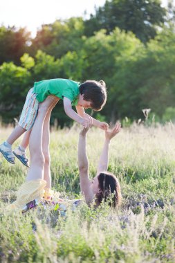 Anne oğlu aktif oyunlar oynuyor. Jimnastik alanında bir çocukla. Çocuk Anne bacaklarına yalan söylüyor. Kadın bebek ayağa yükseltir. Çimenlerin üzerinde bir çift yoga. Akroyoga.