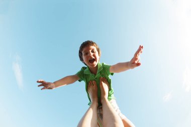 Çocuk bir uçak gibi annemin bacaklarına uçar. Çocuk gökyüzüne karşı. Çocuk ve anne doğada Yoga nişanlandık. Bir kadın oğlunu eğlendirir.