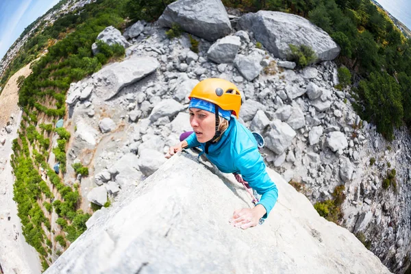 Mountaineer in helmet. A woman climbs the rock. The girl is engaged in extreme sports in nature. Insurance and safety in climbing. Overcoming a difficult climbing route.