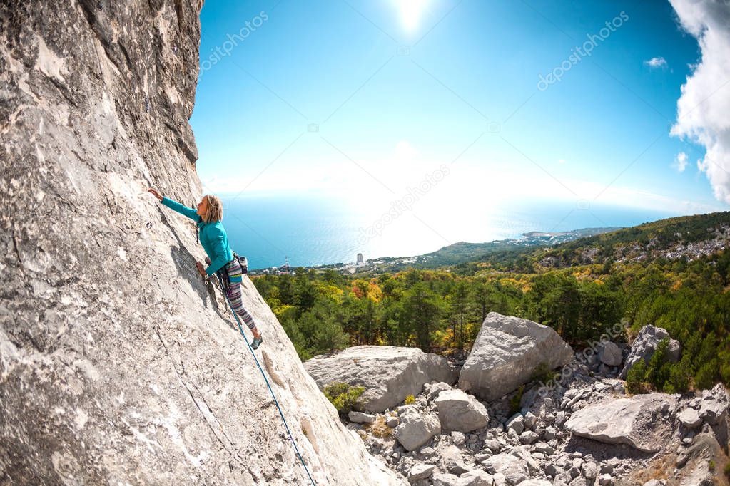 Rock climber on a rock. Girl climbs the rock on the background of a beautiful mountain landscape and the sky with clouds. Active lifestyle. Sports in nature. Overcoming a difficult climbing route.