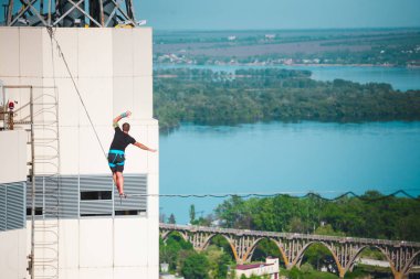 Bir adam bir hat boyunca yürüyor. Dört iki yüksek binalar arasında sıkı bir çizgi izler. Highline şehir ve nehir arka planı.